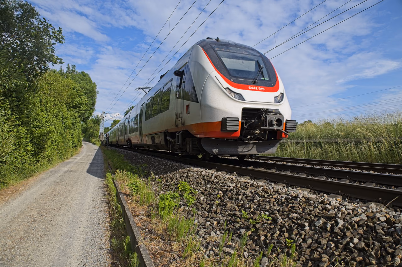 A passenger train moving along a railroad track under a blue sky