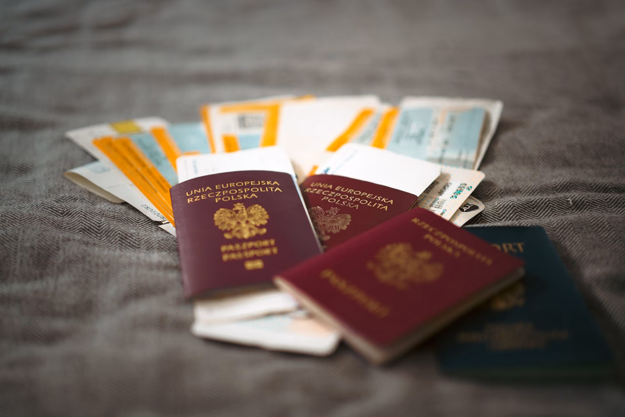 Three passports and a fan of paper boarding passes spread on a gray woven blanket