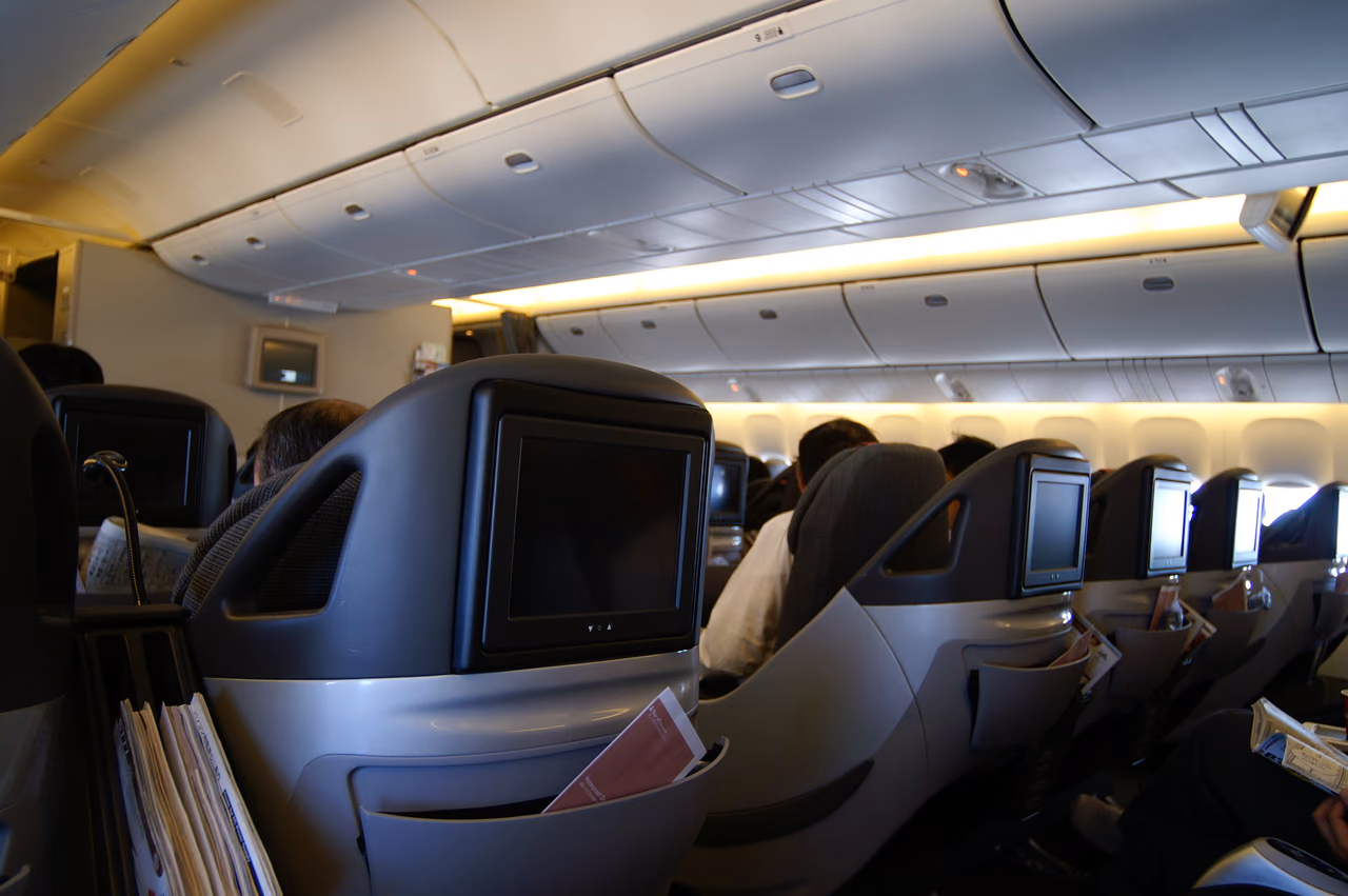 Rows of grey shell-style premium cabin seats with seatback screens and reading lights in a wide-body aircraft