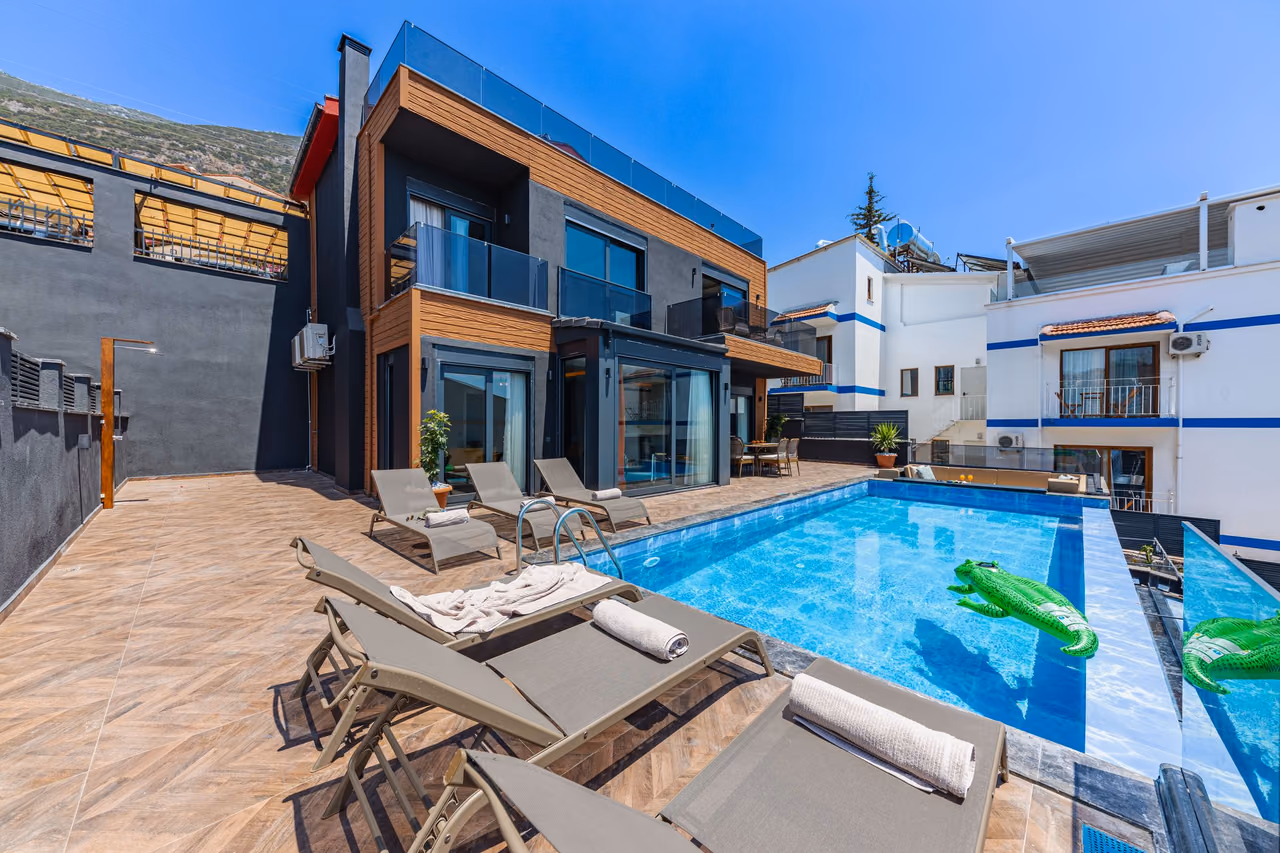A modern rental villa with a private pool, gray sun loungers with rolled white towels and inflatable crocodile floats