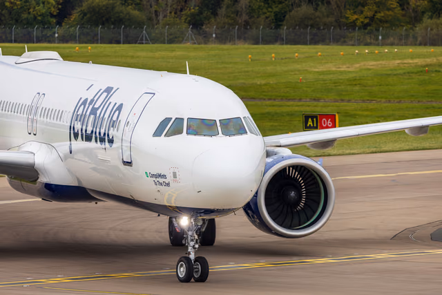 A JetBlue Airbus taxiing on an airport runway with green hills behind it