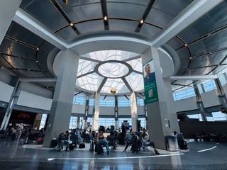 Travelers with luggage seated in a gate area beneath a domed skylight in Terminal 2 at San Diego International Airport