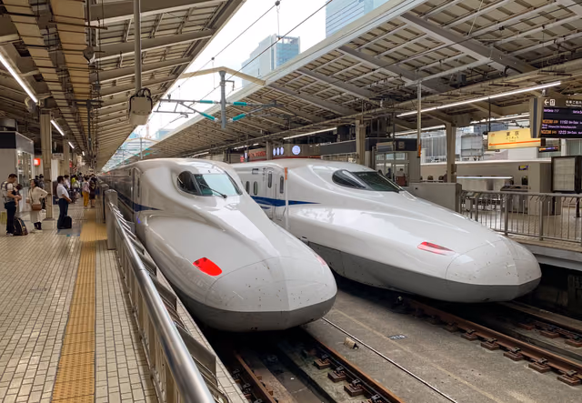 Two white Shinkansen bullet trains stopped side by side at a Tokyo Station platform, with passengers waiting beside the nearest train