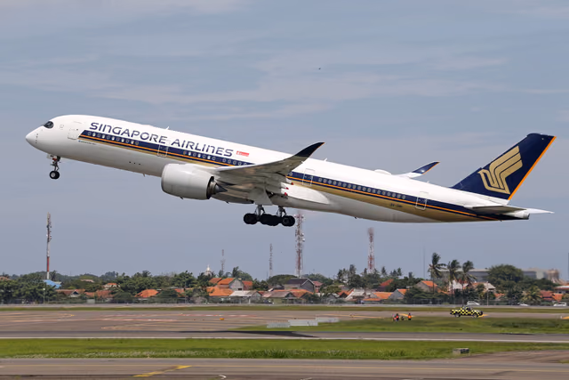 A Singapore Airlines Airbus A350 lifting off a runway with houses in the background