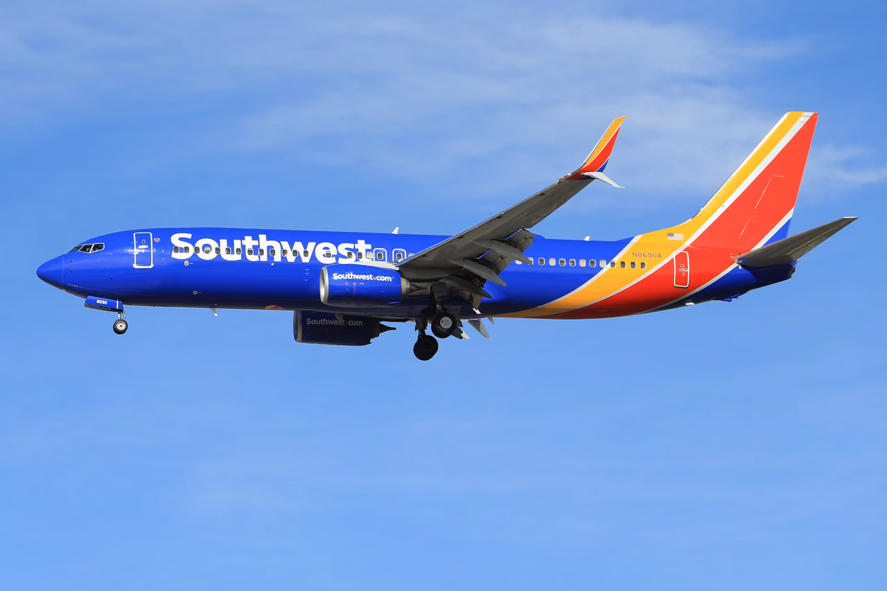 Southwest Airlines Boeing 737 in blue, red and yellow livery flying with its landing gear down under a pale blue sky with thin clouds