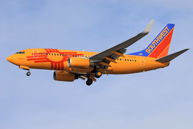 A Southwest Airlines Boeing 737 in an orange special livery flying against a clear blue sky