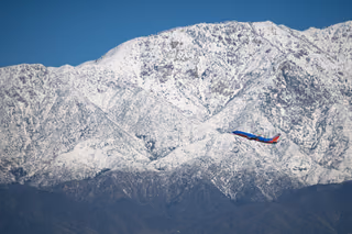 A Southwest Airlines Boeing 737 in blue and red livery climbing past snow-covered mountains under a clear blue sky
