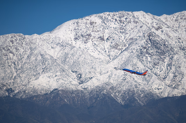 A Southwest Airlines Boeing 737 in blue and red livery climbing past snow-covered mountains under a clear blue sky