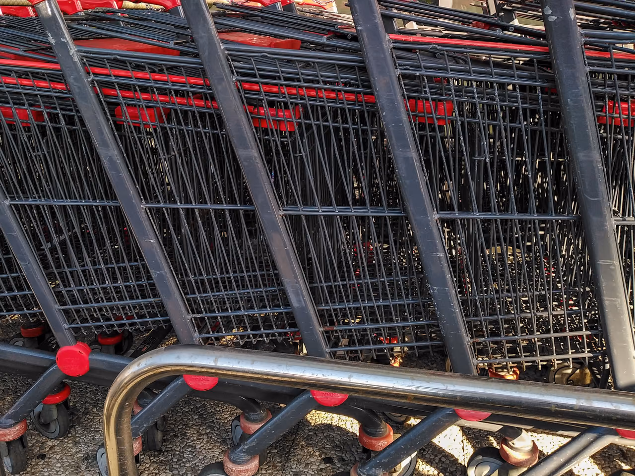 Row of stacked metal shopping carts with red handles and red wheels, parked outdoors in bright sun
