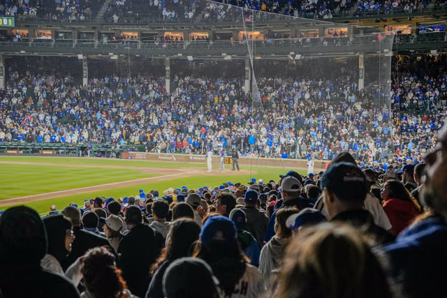 A packed baseball stadium at night, with fans filling the stands under bright lights during a game