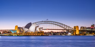 The Sydney Opera House and the Sydney Harbour Bridge at dusk, lit up across the water under a deep blue sky