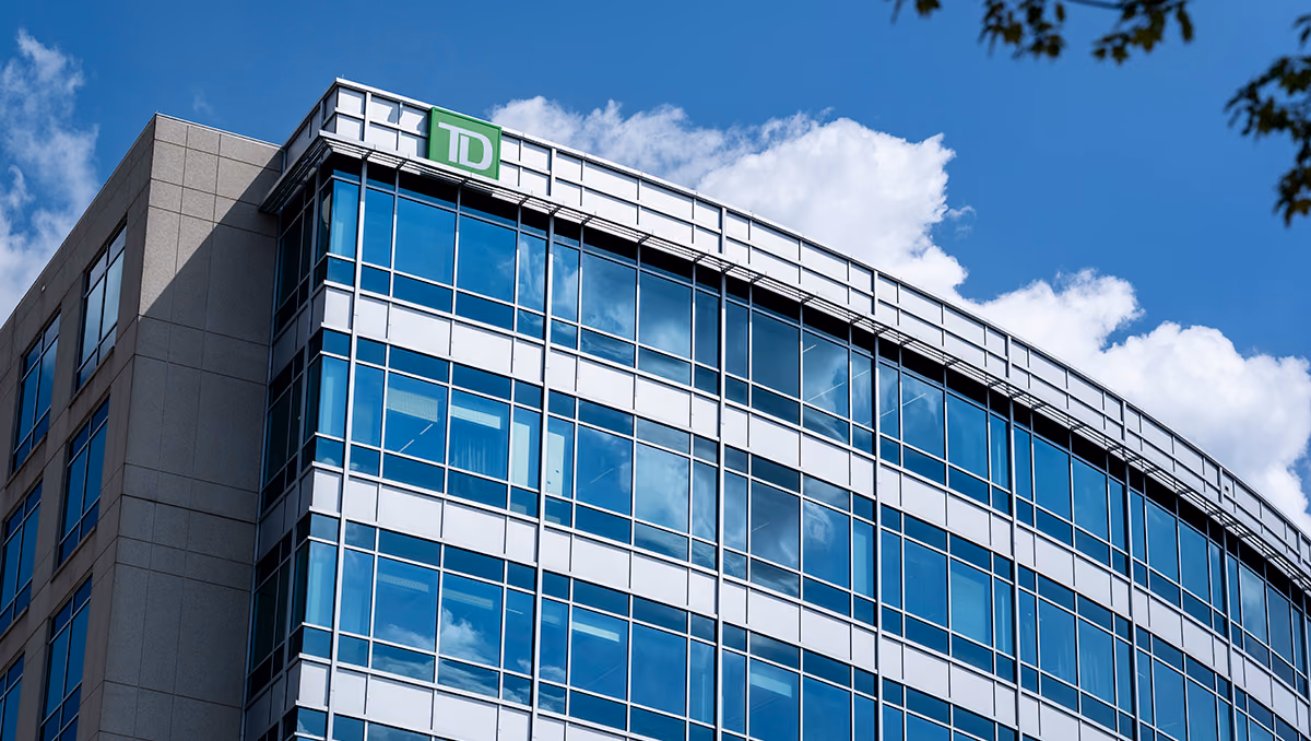 A glass office building with a green TD logo near the roofline, under a blue sky with white clouds