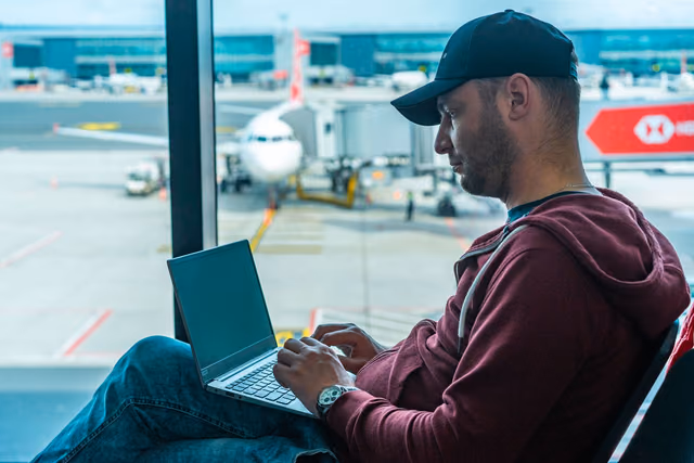 Traveler working on a laptop in an airport terminal with a plane visible outside