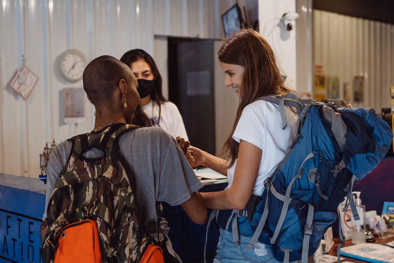 Two travelers with backpacks checking in together at a hotel front desk