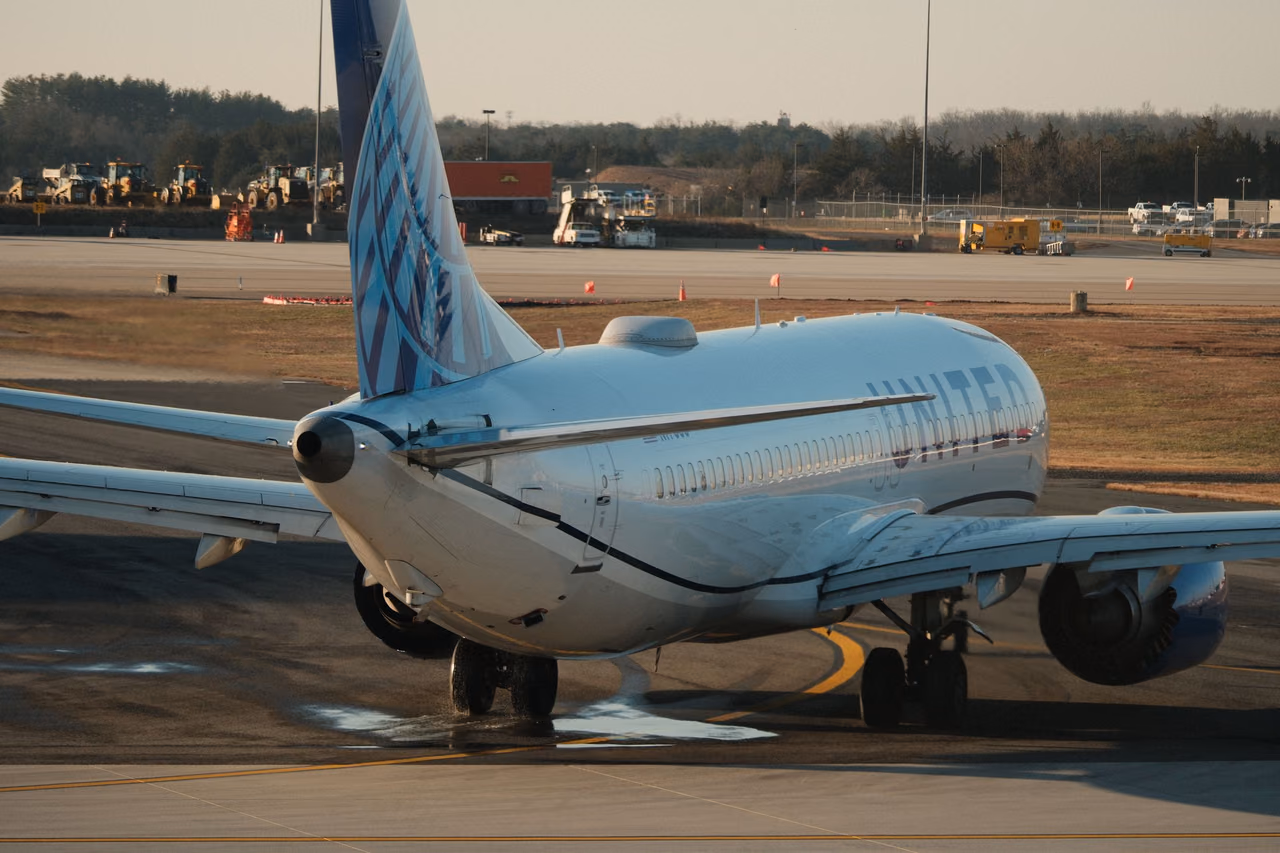 A United Airlines jet taxiing on an airport apron in low evening sun, seen from behind the tail