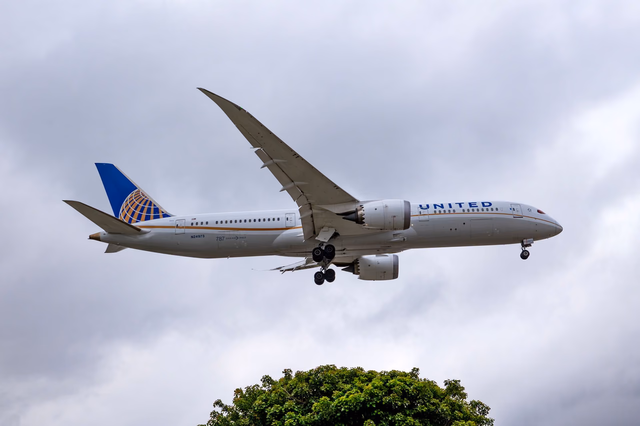 A United Airlines Boeing 787 Dreamliner in flight with its landing gear down on approach to land, under a cloudy gray sky