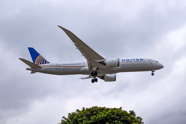 A United Airlines Boeing 787 Dreamliner in flight with its landing gear down on approach to land, under a cloudy gray sky