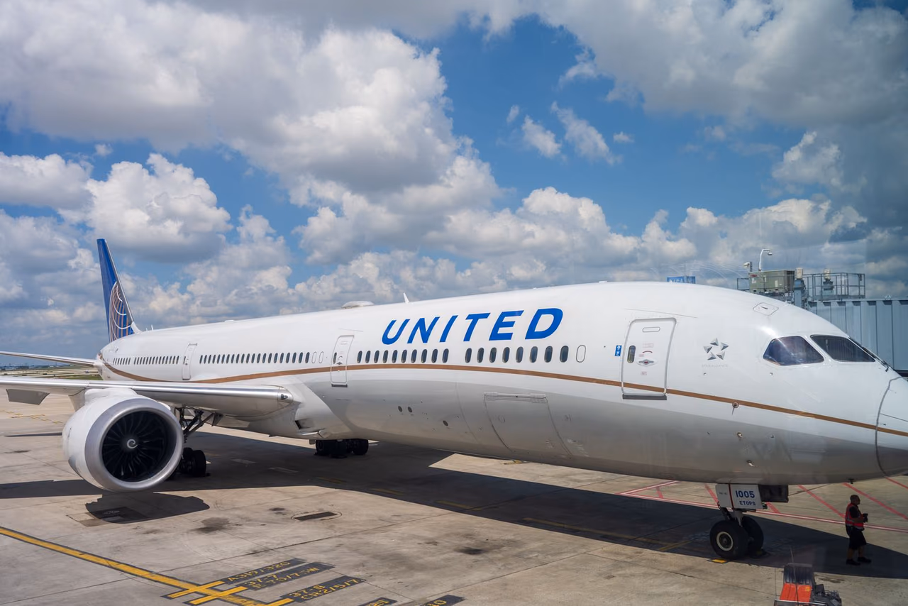 United Airlines Boeing 787 parked at an airport terminal gate under a blue sky with clouds