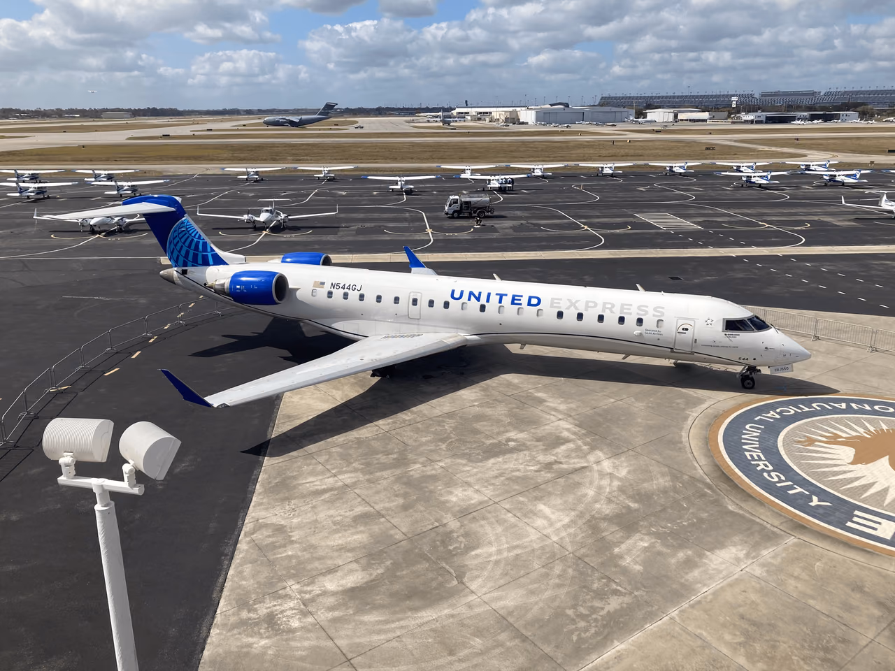 White United Express Bombardier CRJ-550 regional jet with a blue tail on an airport ramp, small training aircraft behind