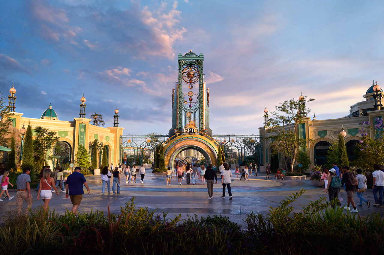 Celestial Park's ornate green and gold entry archway and tower at Universal Epic Universe at dusk, with guests walking across the plaza