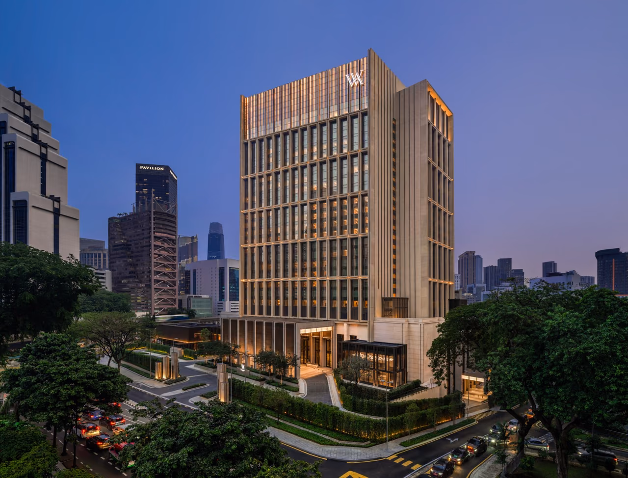 Waldorf Astoria Kuala Lumpur tower lit at dusk, with a landscaped entrance drive and the city skyline behind it