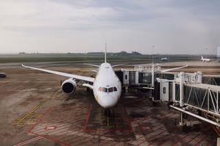 A white widebody jet parked at a terminal jet bridge on an overcast day, seen from the airport window