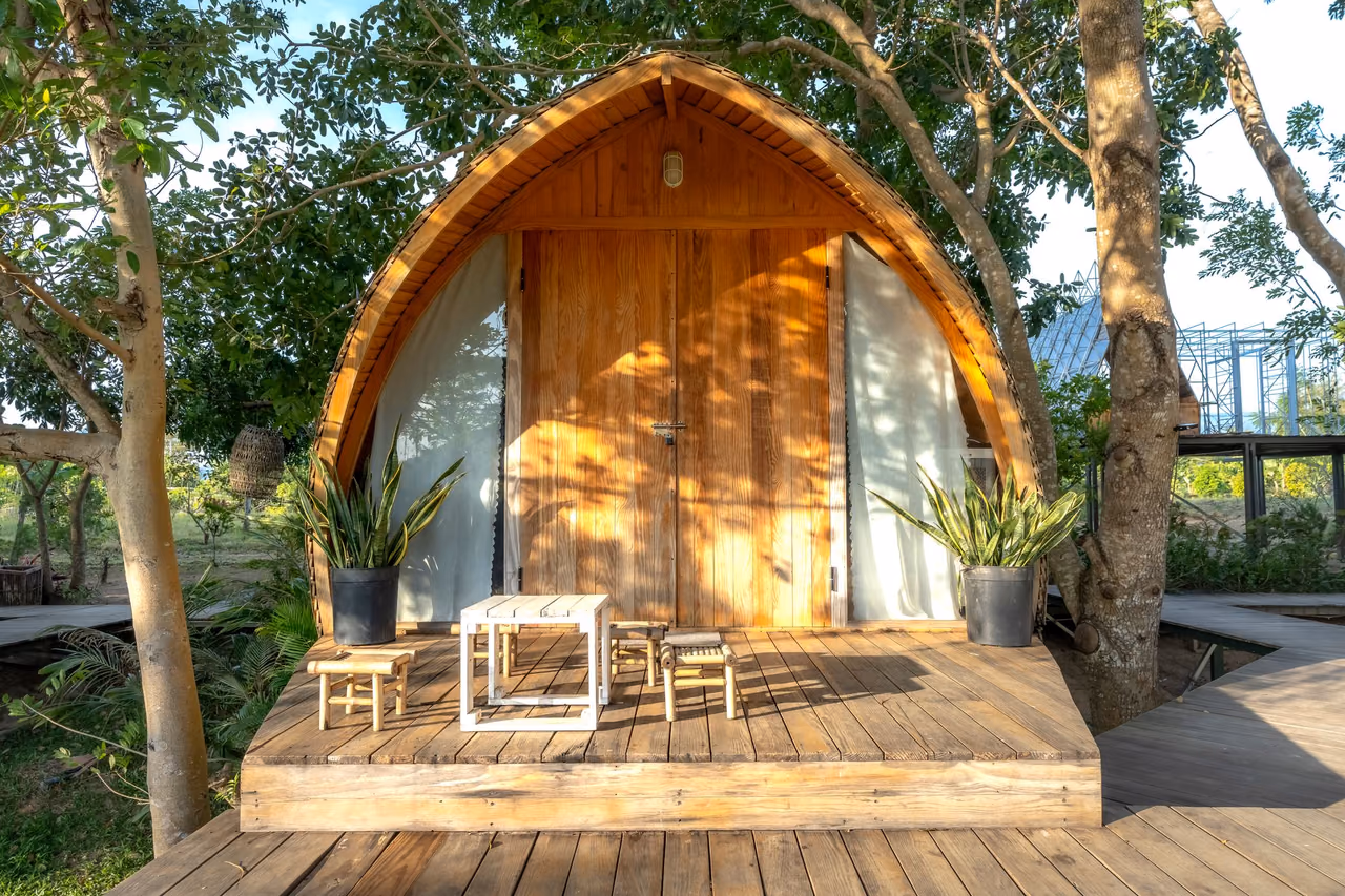 Wooden vacation cabin with a small patio set among green trees in daylight
