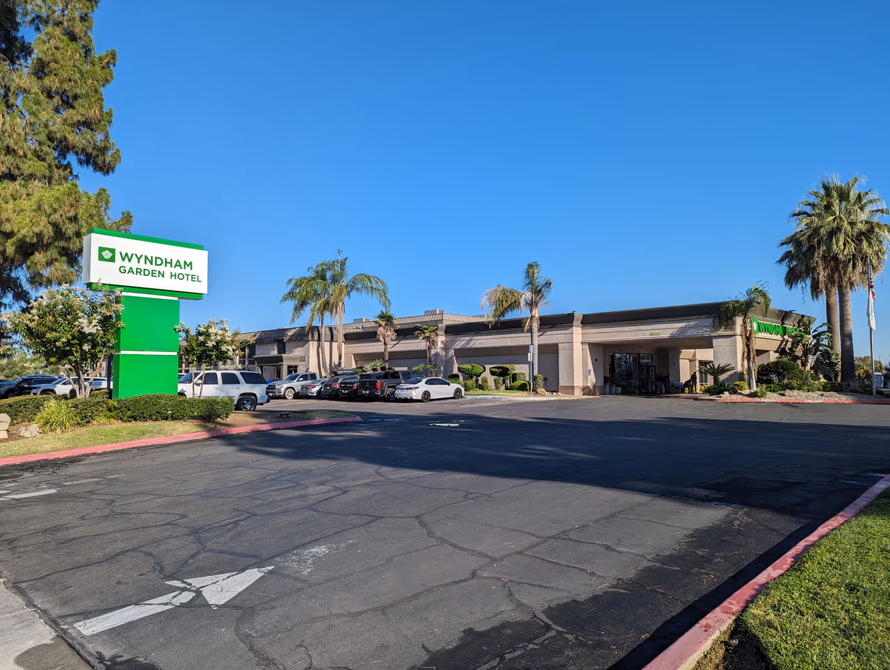 A low-rise Wyndham Garden hotel building with a porte-cochere entrance and palm trees against a clear sky